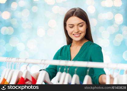 clothing, fashion, style and people concept - happy woman choosing clothes at wardrobe over blue holidays lights background