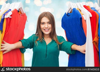 clothing, fashion, style and people concept - happy woman choosing clothes at wardrobe over blue holidays lights background