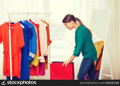 clothing, fashion, style and people concept - happy woman with shopping bags and clothes at home wardrobe. happy woman with shopping bags and clothes at home