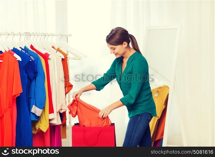 clothing, fashion, style and people concept - happy woman with shopping bags and clothes at home wardrobe. happy woman with shopping bags and clothes at home