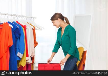 clothing, fashion, style and people concept - happy woman with shopping bags and clothes at home wardrobe