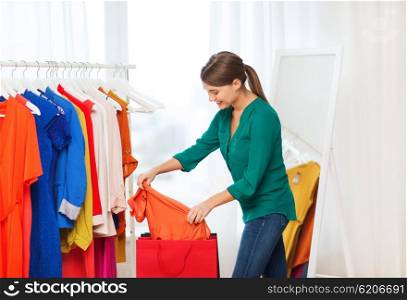 clothing, fashion, style and people concept - happy woman with shopping bags and clothes at home wardrobe