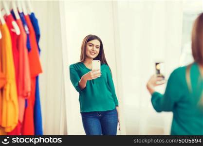 clothing, fashion, style, technology and people concept - happy woman with smartphone taking mirror selfie at home wardrobe. woman with smartphone taking mirror selfie at home