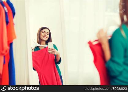 clothing, fashion, style, technology and people concept - happy woman with smartphone snd red dress taking mirror selfie at home wardrobe. woman with smartphone taking mirror selfie at home