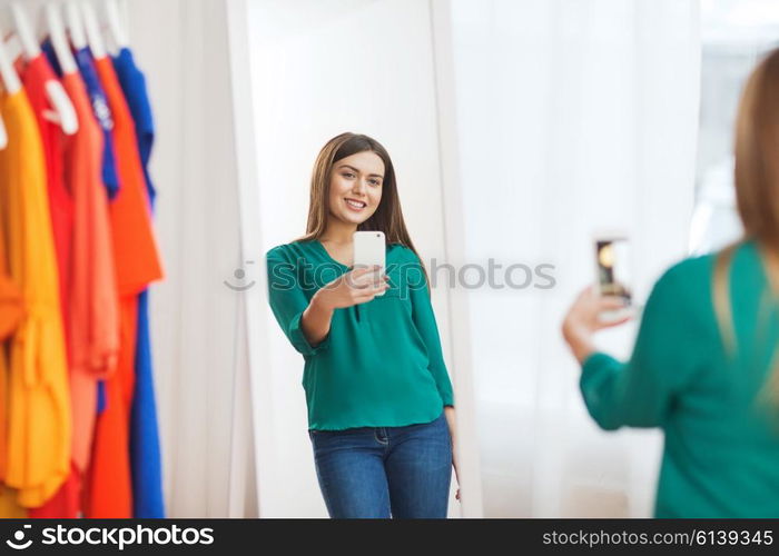 clothing, fashion, style, technology and people concept - happy woman with smartphone taking mirror selfie at home wardrobe