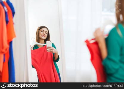 clothing, fashion, style, technology and people concept - happy woman with smartphone snd red dress taking mirror selfie at home wardrobe