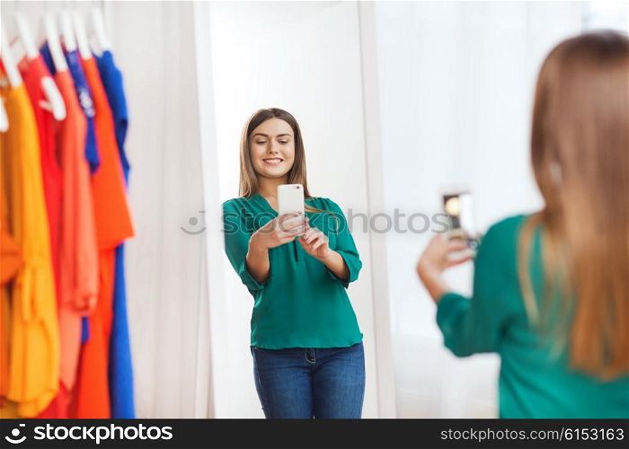 clothing, fashion, style, technology and people concept - happy woman with smartphone taking mirror selfie at home wardrobe