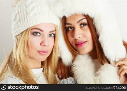 Clothing people fashion concept. Two ladies in winter outfit. Blonde woman together with mulatto girl, wearing white warm clothes.. Two ladies in winter white outfit.