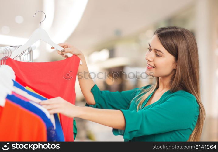 clothing, sale, fashion, style and people concept - happy woman choosing clothes at shopping center or mall