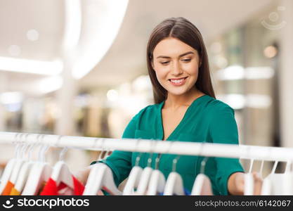 clothing, sale, wear and people concept - happy woman choosing clothes at shopping center or mall