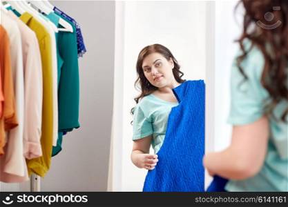clothing, wardrobe, fashion, style and people concept - happy plus size woman with dress on hanger at mirror at home