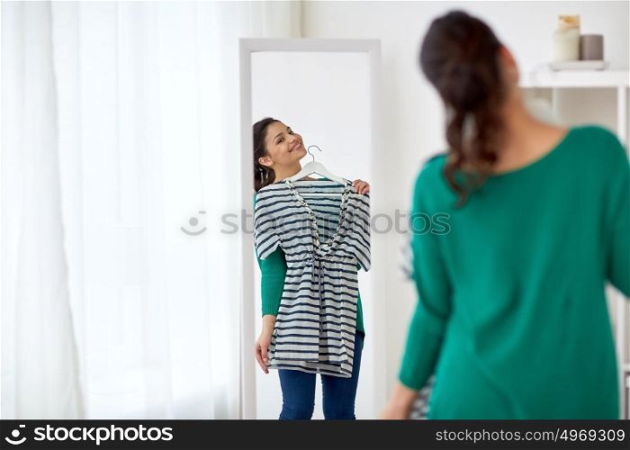 clothing, wardrobe, fashion, style and people concept - happy woman with shirt looking to mirror at home. happy woman with shirt looking to mirror at home