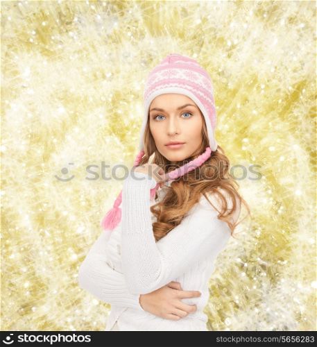 clothing, winter holidays, christmas and people concept - smiling young woman in hat and sweater over yellow lights background