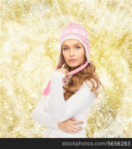 clothing, winter holidays, christmas and people concept - smiling young woman in hat and sweater over yellow lights background