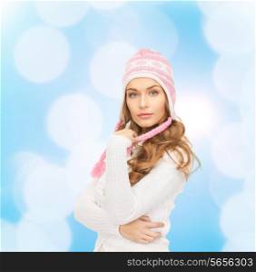 clothing, winter holidays, christmas and people concept - smiling young woman in hat and sweater over blue lights background