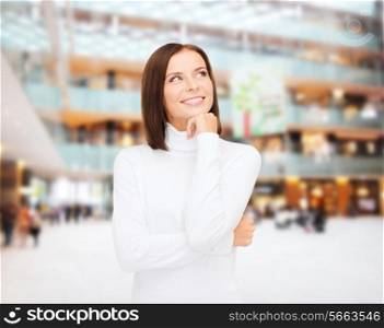clothing, winter holidays, christmas and people concept - smiling young woman in white sweater over shopping center background