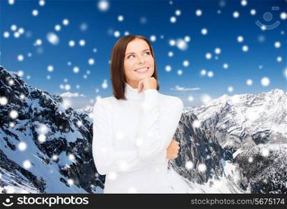 clothing, winter holidays, christmas and people concept - smiling young woman in white sweater over snowy mountains background