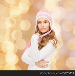 clothing, winter holidays, christmas and people concept - smiling young woman in hat and sweater over beige lights background