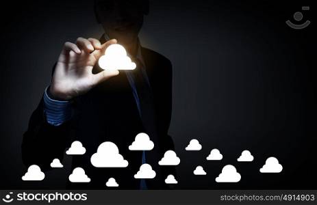 Cloud computing concept. Businessman on dark background taking cloud icon with fingers