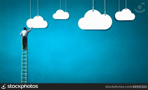 Cloud computing. Rear view of businessman standing on ladder and reaching cloud