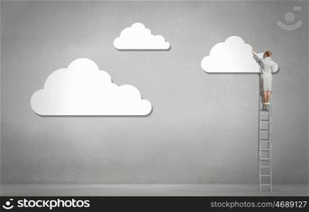 Cloud concept. Back view of businesswoman standing on ladder and reaching to cloud