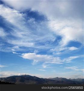 Cloud formations against blue sky with mountain range off in the distance.