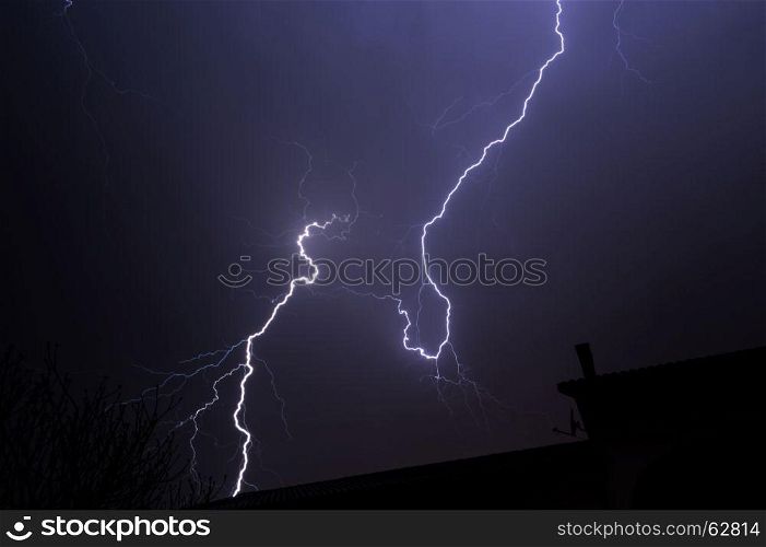 Cloud to ground electric lightning behind house roof top.