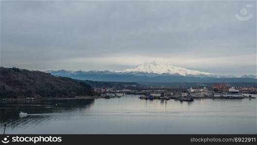 Clouds cover the top part of a snow-laden Mount Rainier. Port of Tacoma is below.