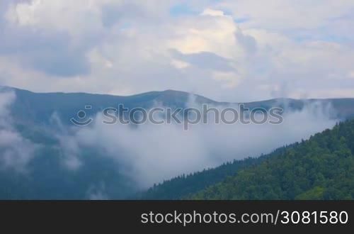 Clouds moving over mountains and village in summer day panoramic view.