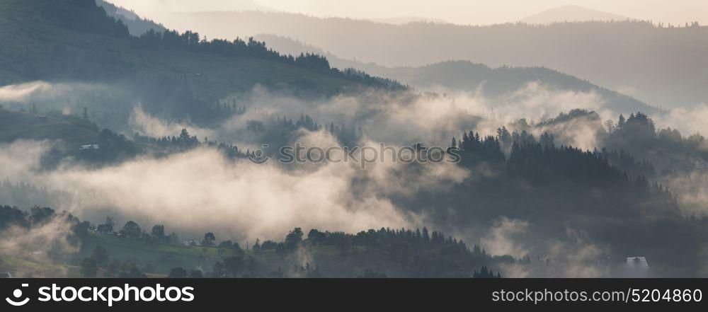 Clouds of fog after rain in evening sunset. Misty village on the pass panorama. Mountain landscape after storm.