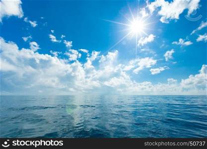 clouds on blue sky over calm sea with sunlight reflection