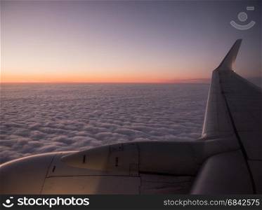 cloudscape with colorful sundown seen behind wing of airplane