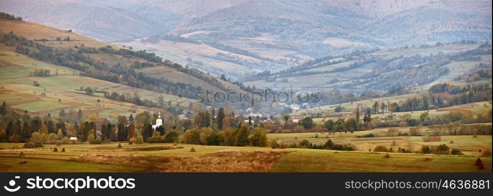 Cloudy autumn panorama in mountain hills. Village in October valley