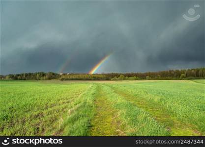 Cloudy sky with a fragment of a rainbow and a green meadow, Czulczyce, Poland