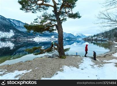 Cloudy winter Alpine lake Grundlsee view (Austria) with fantastic pattern-reflection on water and family on shore.
