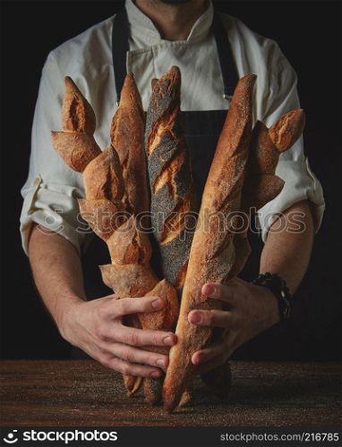 Clous up hands man holding baguettes on a wooden table. Hands of man holding baguettes