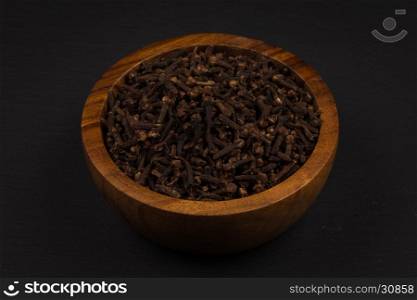 Clove spice in wooden bowl on dark stone plate background