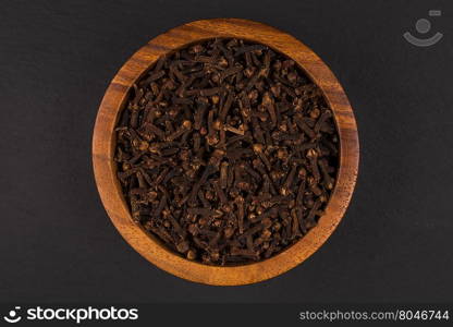 Clove spice in wooden bowl on dark stone plate background