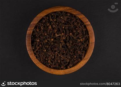 Clove spice in wooden bowl on dark stone plate background