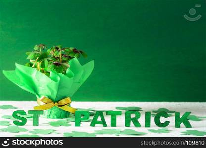 Clover pot wrapped in green paper and golden ribbon and bow and the words St Patrick written in green wooden letters, surrounded by paper shamrock.