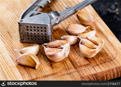 Cloves of garlic on a cutting board with a garlic press. On a black background. High quality photo. Cloves of garlic on a cutting board with a garlic press.