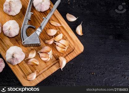 Cloves of garlic on a cutting board with a garlic press. On a black background. High quality photo. Cloves of garlic on a cutting board with a garlic press.