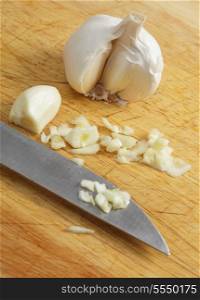 Cloves of garlic, one chopped, the knife and the bulb on a chopping board