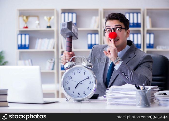 Clown businessman in the office with hammer and an alarm clock