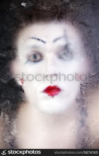 clown face in theatrical makeup through frosty glass