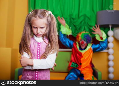 Clown tries to cheer up a sad girl. Playroom on the background.