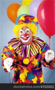 Clown with a bunch of helium balloons, holding a red one toward the camera.