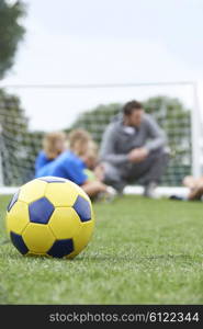 Coach And Team Discussing Soccer Tactics With Ball In Foreground