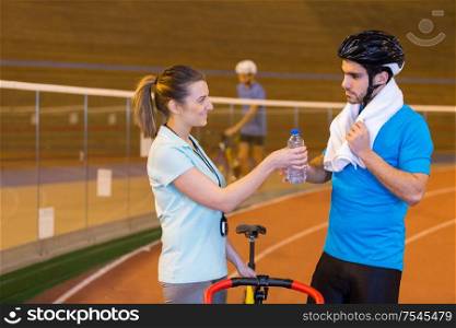 coach passing bottle of water to cyclist in velodrome