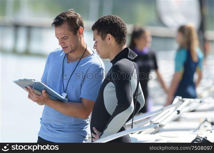 coach with stopwatch and clipboard talking to man in wetsuit